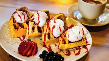 A plate of waffles with whipped cream and syrup, accompanied by a cup of coffee and fresh berries.