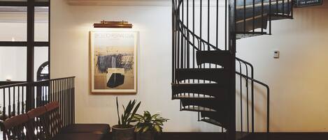 Un interior moderno con una escalera espiral, bancos de madera, plantas en macetas y un cartel enmarcado en la pared.
