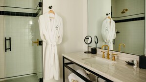 A modern bathroom with a glass shower enclosure, a marble sink with gold fixtures, and a large mirror.