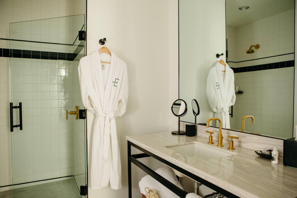 A modern bathroom with a glass shower enclosure, a marble sink with gold fixtures, and a large mirror.