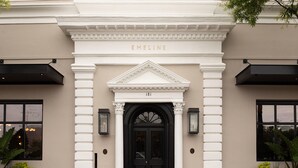 A building facade with a black entrance door, white columns, and the name "EMELINE" above the door.