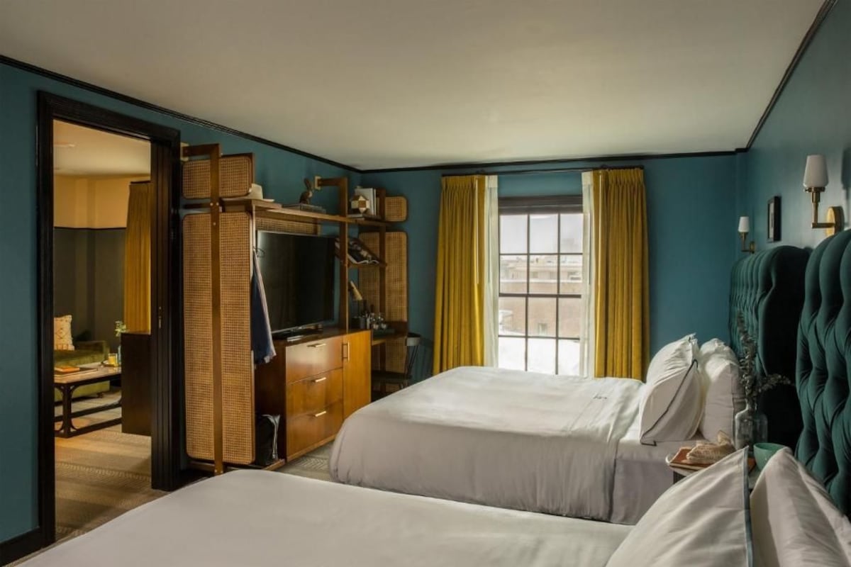Habitación de hotel con dos camas, un escritorio, un armario y una ventana con cortinas.