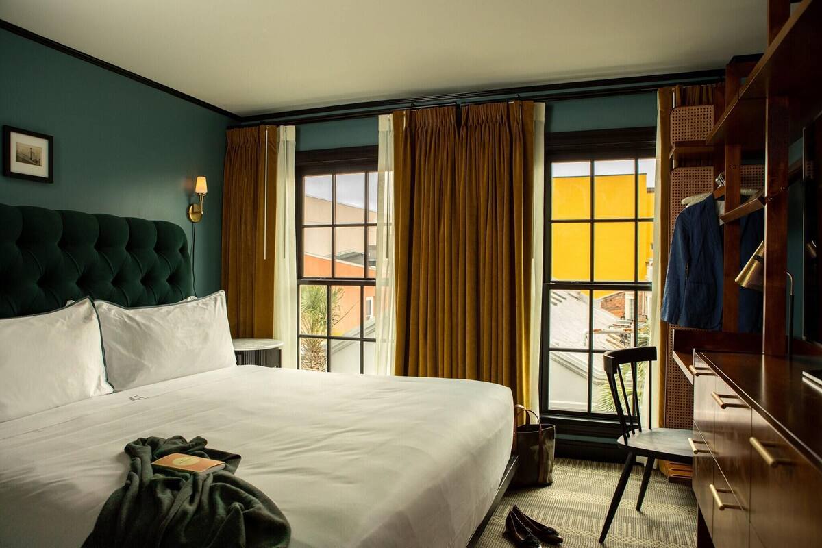 A hotel room with a large bed, a chair, a desk, and a window with curtains.