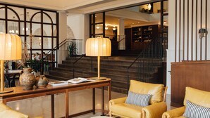A lobby with a wooden table, two yellow leather armchairs, a lamp, and a staircase leading to an upper level.