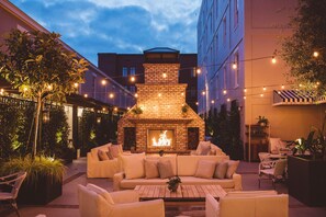 An outdoor patio area with a brick fireplace, white sofas, and string lights. - Emeline (Charleston)
