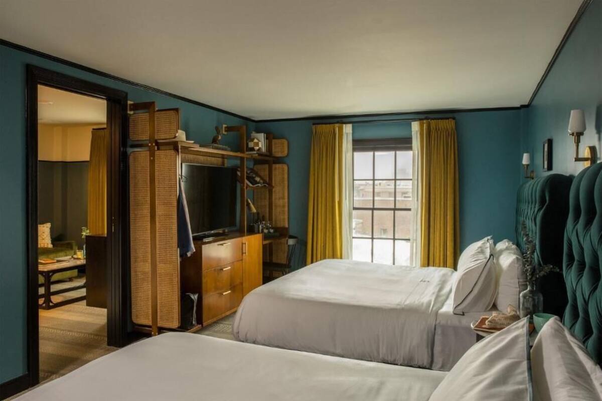 A hotel room with two beds, a desk, a wardrobe, and a window with curtains.