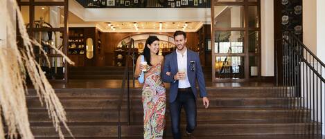 Una pareja caminando por una escalera de madera en el vestíbulo de un hotel, con una decoración moderna y vistas al piso superior.