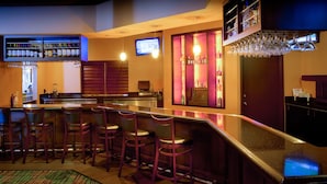 A bar area with a long counter, multiple bar stools, and shelves stocked with bottles.