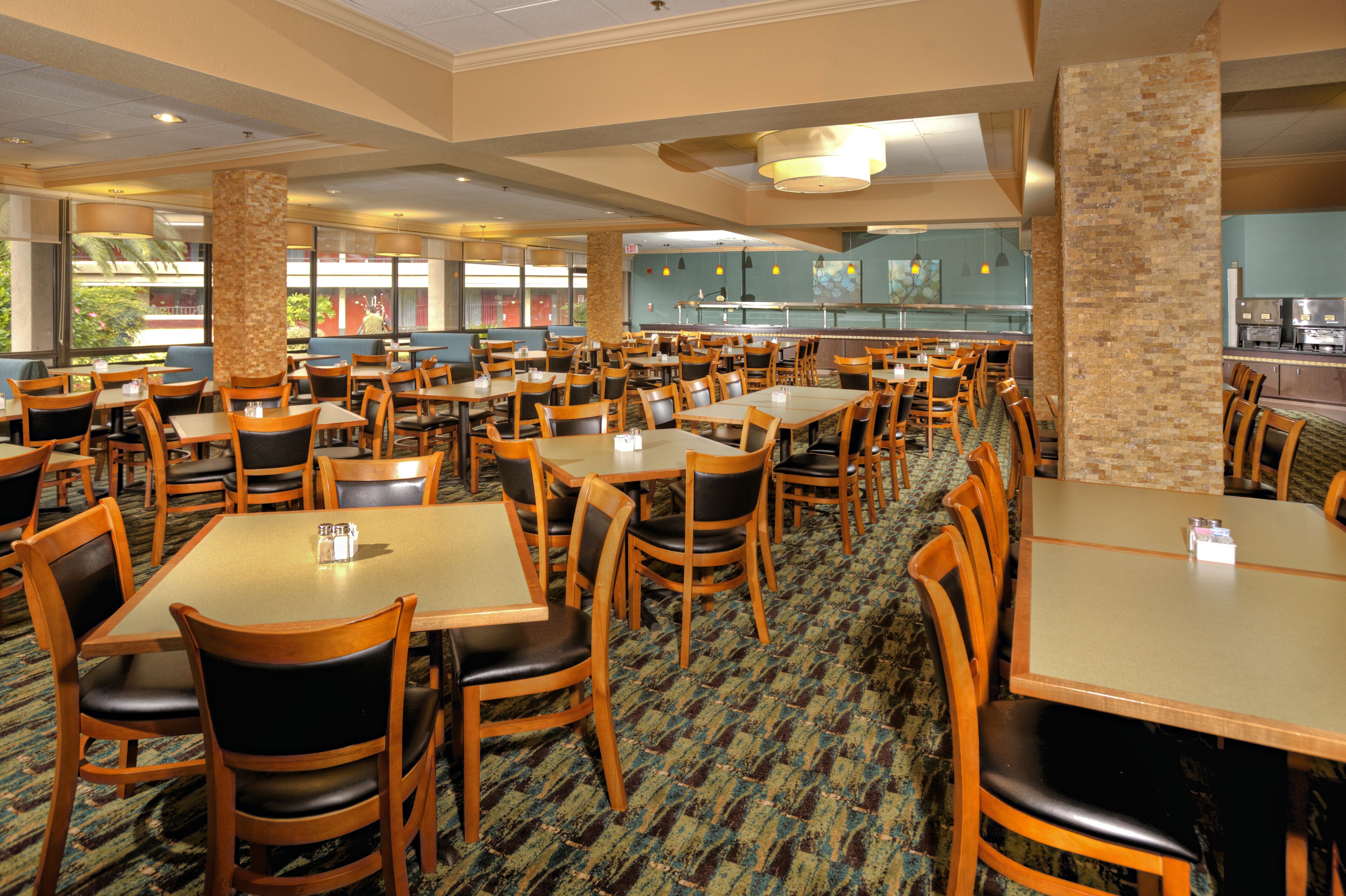 A spacious dining area with multiple tables and chairs, a patterned carpet, and a view of the outside through large windows.