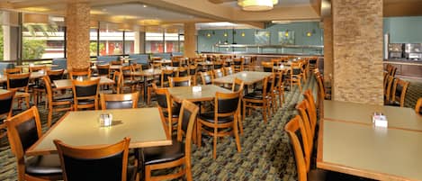 A spacious dining area with multiple tables and chairs, a patterned carpet, and a view of the outside through large windows.