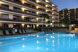 A hotel with a swimming pool, multiple balconies, and outdoor seating areas.
