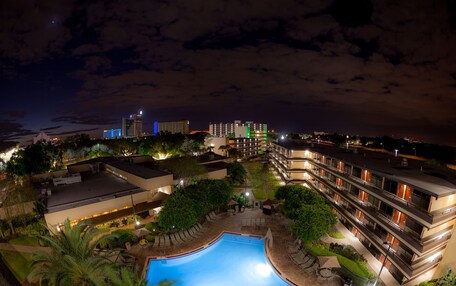 A hotel with a swimming pool, outdoor seating, and a view of the city skyline at night.