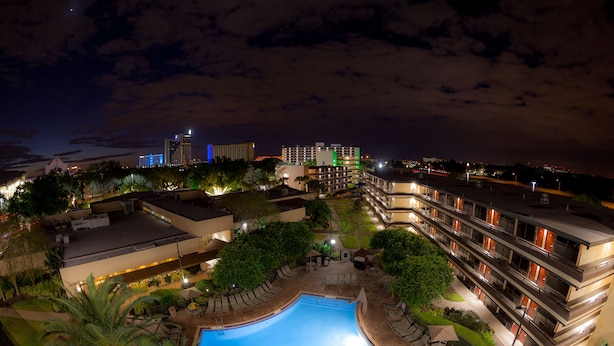A hotel with a swimming pool, outdoor seating, and a view of the city skyline at night.