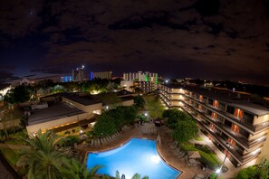 Un hotel con piscina, area salotto esterna e vista sullo skyline cittadino di notte.