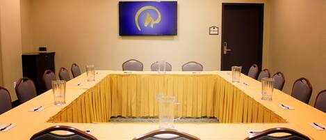 Un salón de conferencias con una larga mesa, sillas y una pantalla grande en la pared.