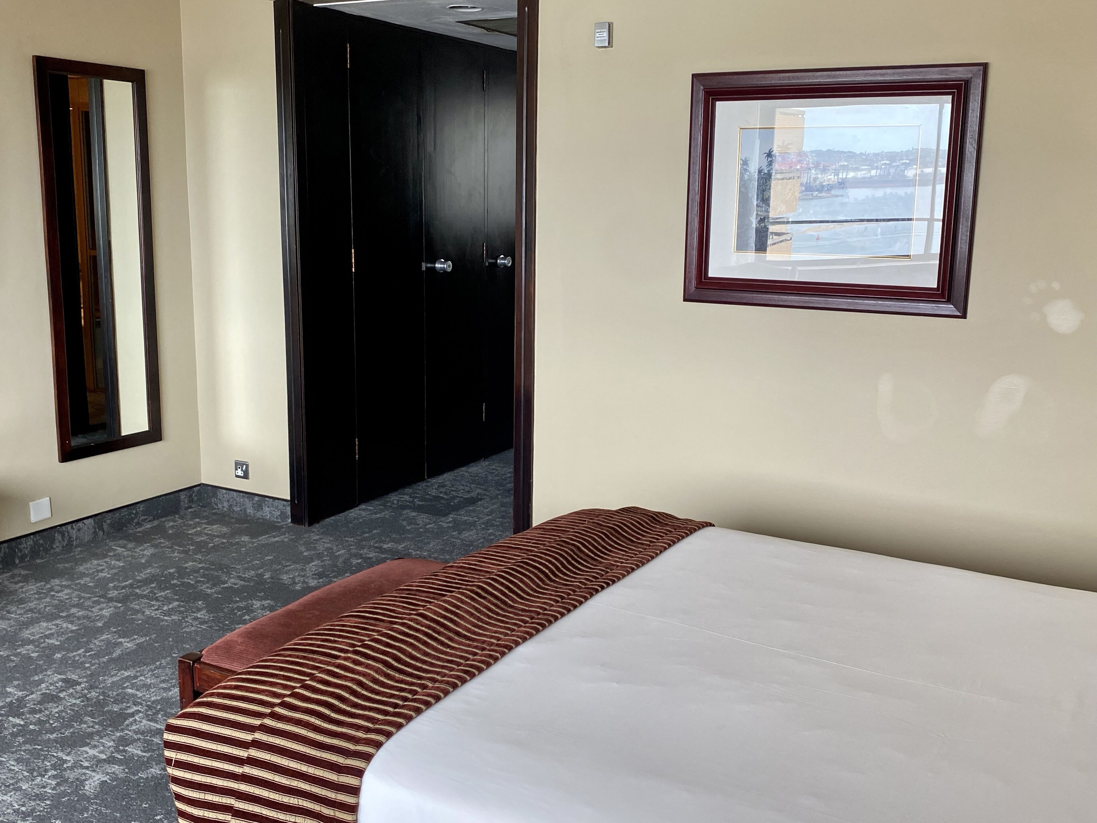 A hotel room with a bed, a large mirror, a wardrobe, and a window with a view.