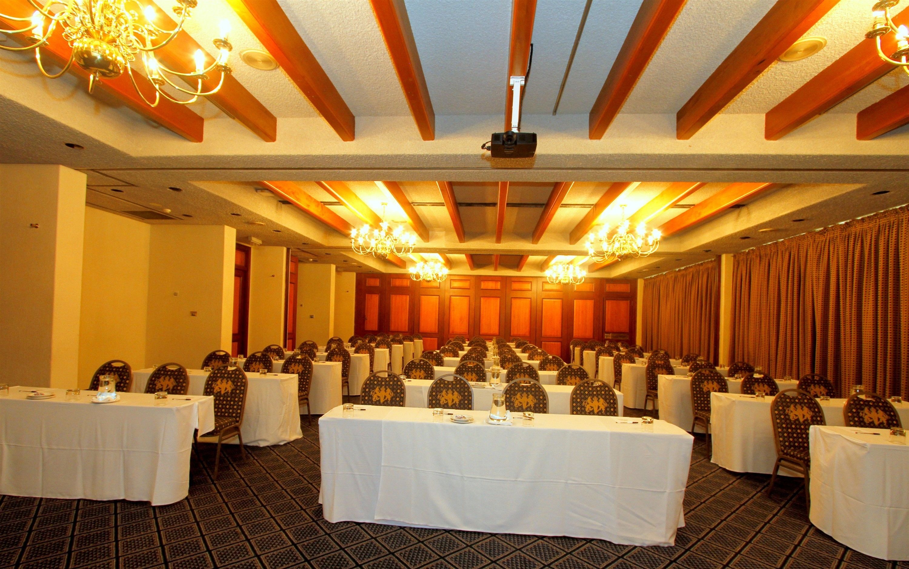 Un salón de banquetes con varias mesas redondas cubiertas de manteles blancos, dispuestas en filas.