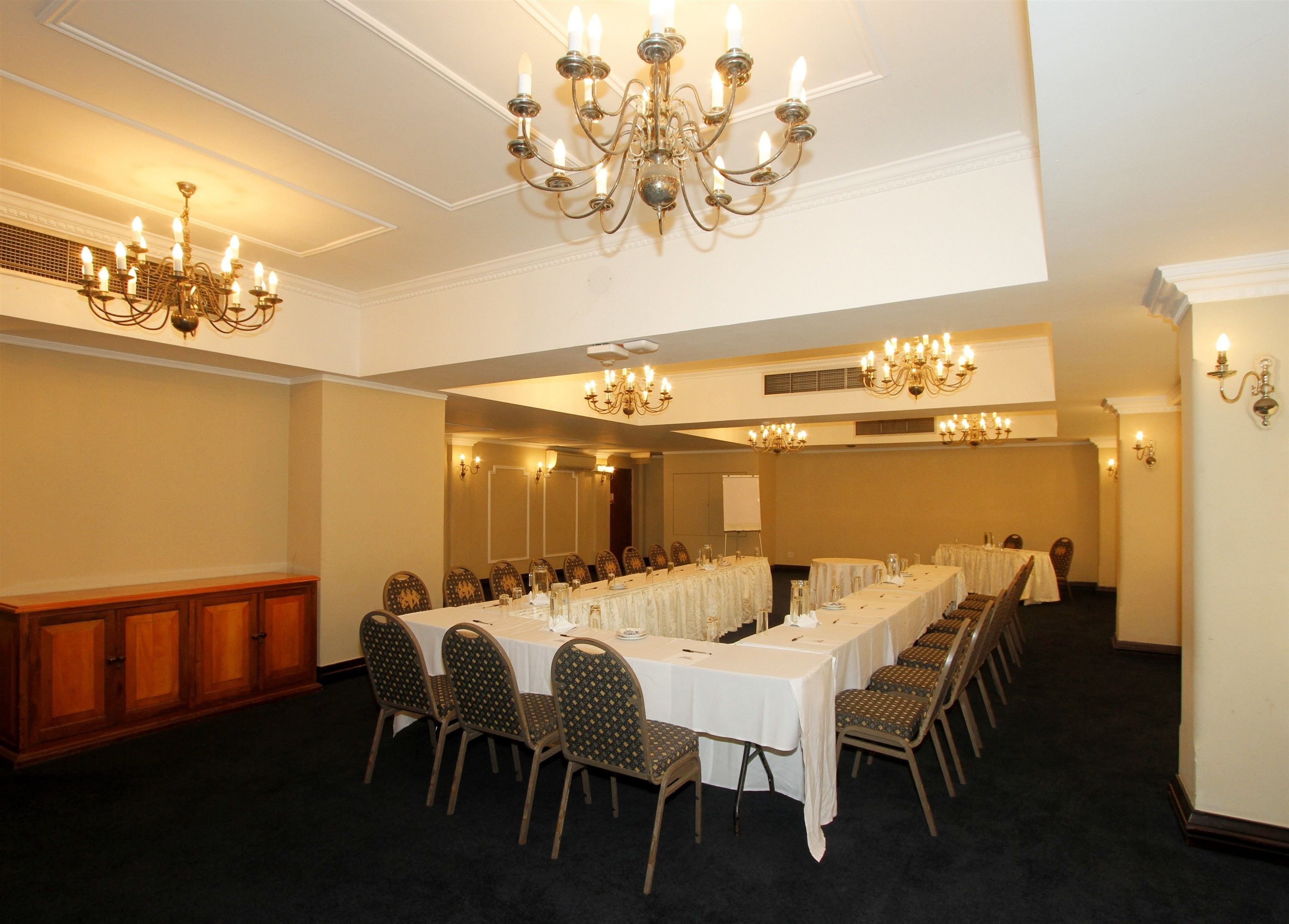 Un salón de conferencias con largas mesas, sillas, candelabros y apliques de pared.