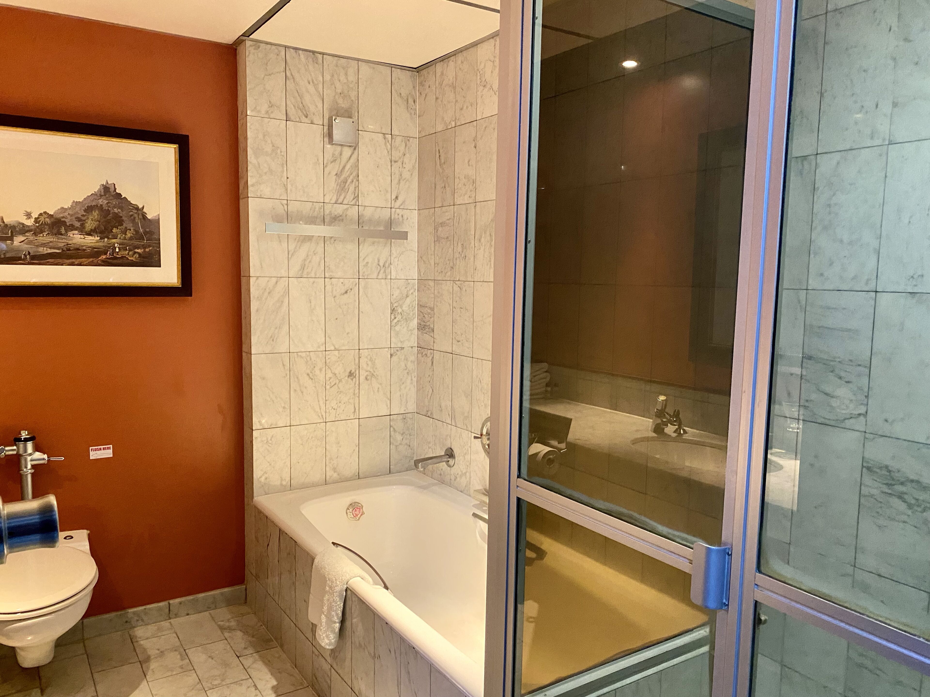 Un baño con ducha de mármol, bañera, inodoro y un cuadro enmarcado en la pared.