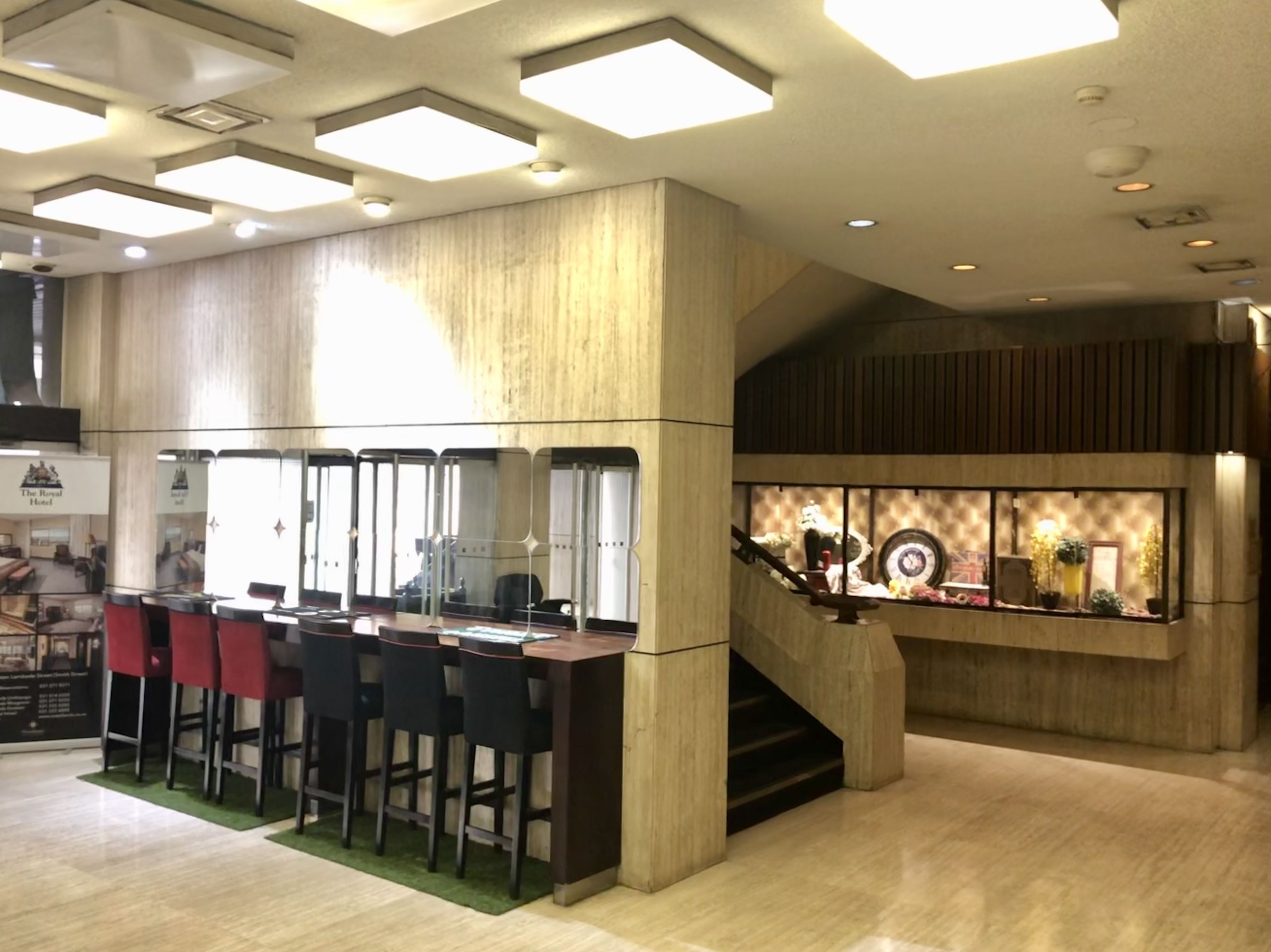 A modern hotel lobby with a bar area, wooden paneling, and a staircase leading to an upper level.