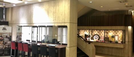 A modern hotel lobby with a bar area, wooden paneling, and a staircase leading to an upper level.