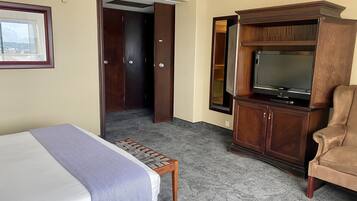 Ein Hotelzimmer mit einem Bett, einem Holzschrank mit Fernseher, einem Sessel und einem Kleiderschrank.