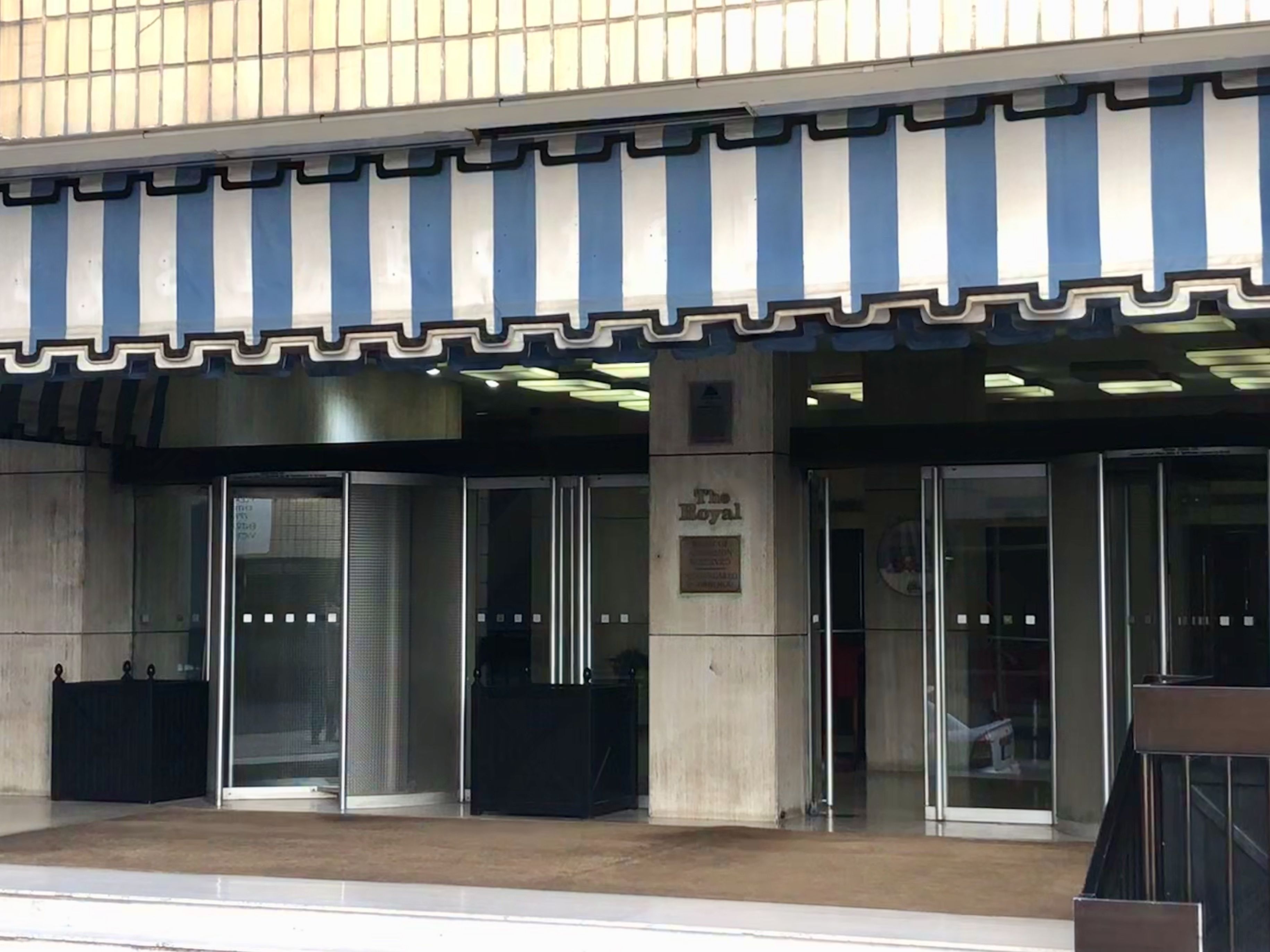 A building with a blue and white striped awning, glass doors, and a plaque that reads "The Royal."