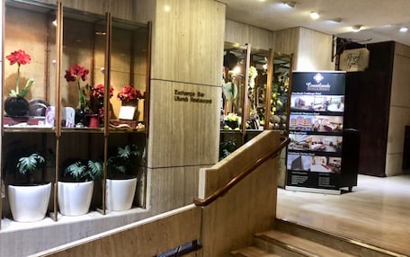 A hotel reception area with a wooden staircase, potted plants, and a sign for the Exchange Bar and Ulundi Restaurant.