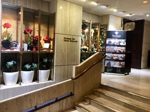 A hotel reception area with a wooden staircase, potted plants, and a sign for the Exchange Bar and Ulundi Restaurant. - The Royal Hotel (Durban)