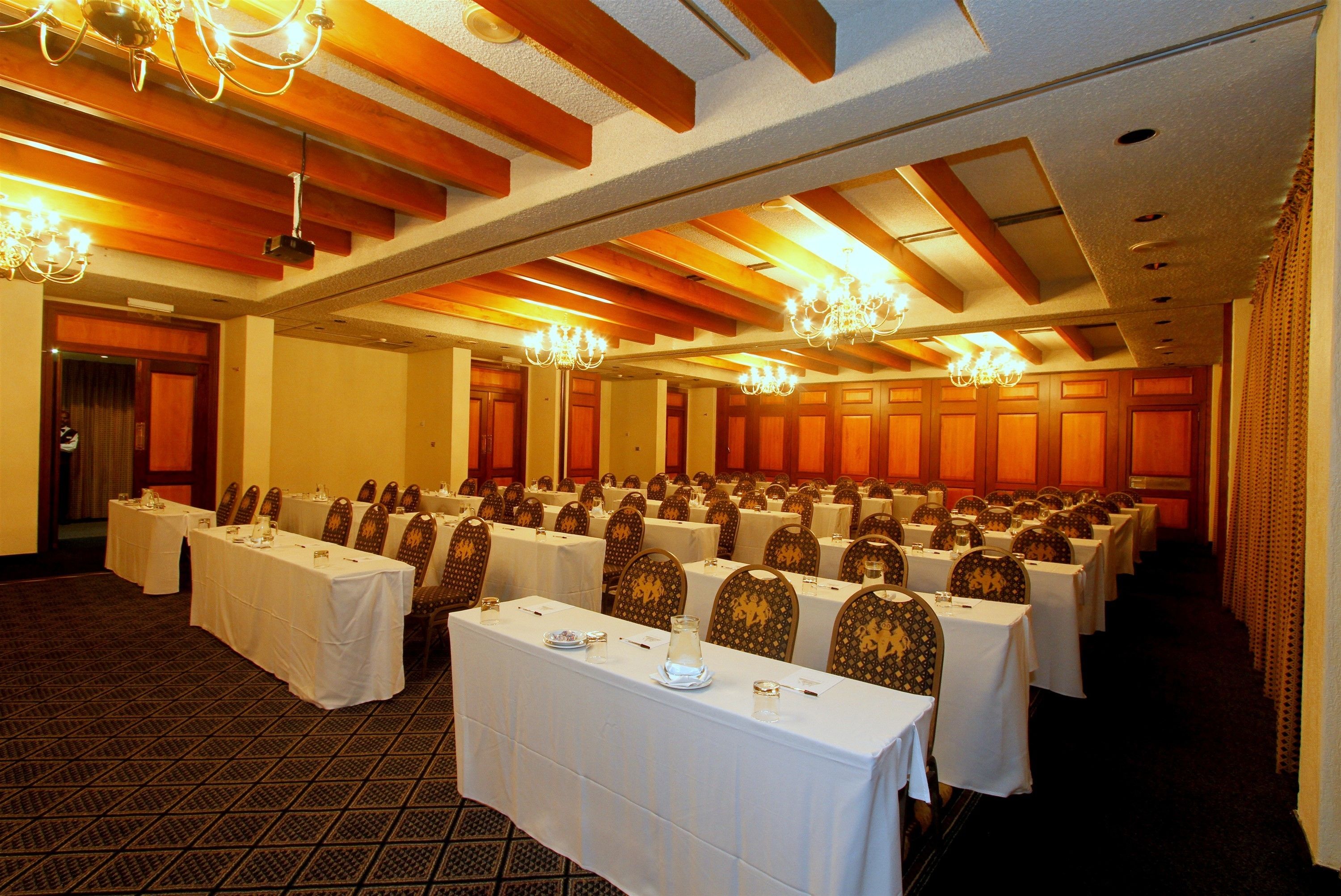 A banquet hall with rows of tables set for dining, wooden paneling on the ceiling, and chandeliers.