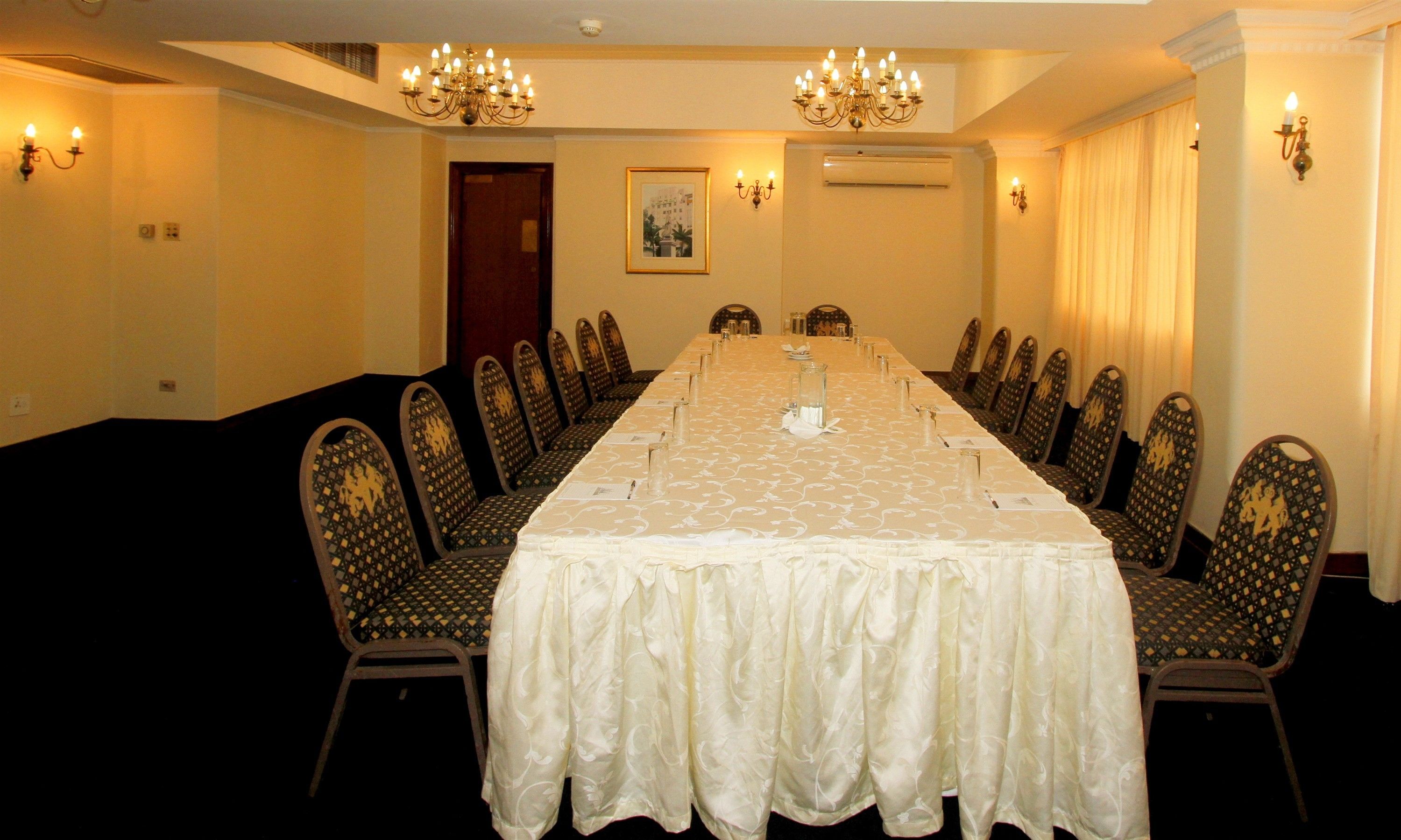 A conference room with a long table, chairs, chandeliers, and wall sconces.
