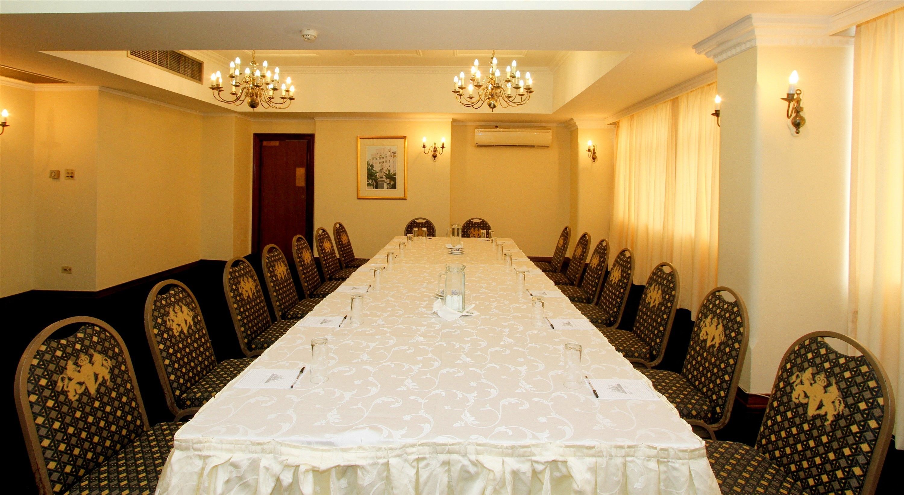 A conference room with a long table, chairs, chandeliers, and wall sconces.
