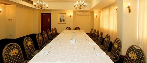 A conference room with a long table, chairs, chandeliers, and wall sconces.