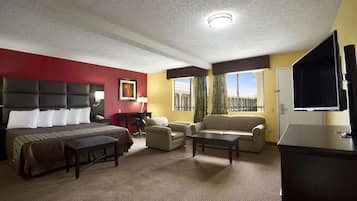 A hotel room with a large bed, a desk, a sofa, a television, and a window with a view.