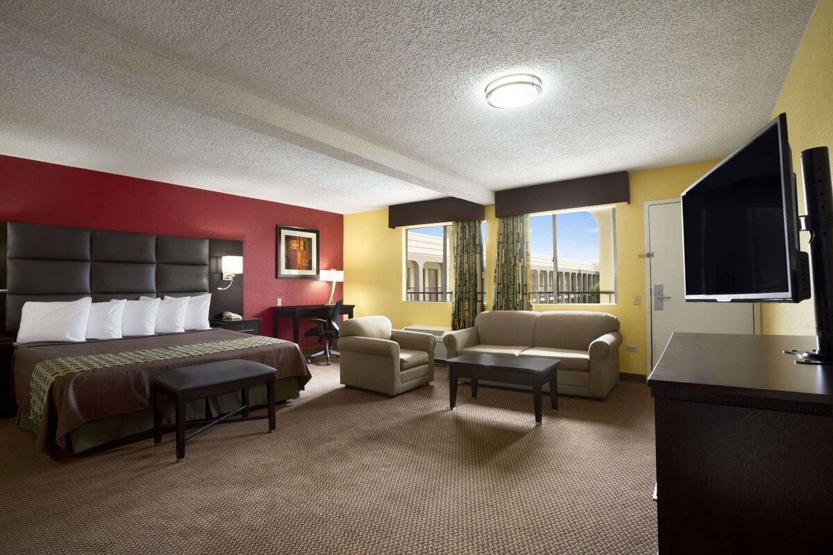 Ein Hotelzimmer mit Bett, Schreibtisch, Sofa, Fernseher und einem Fenster mit Blick.