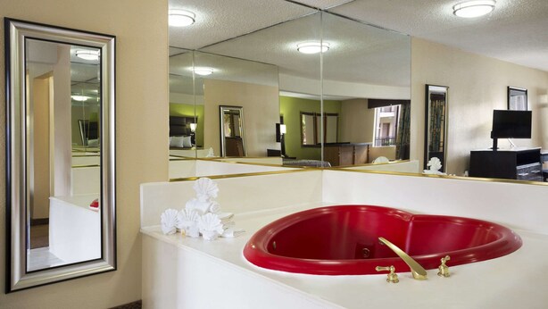Een badkamer met een rood bad, een grote spiegel en een witte wastafel.