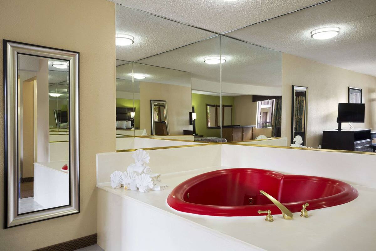 Ein Badezimmer mit einer roten Badewanne, einem großen Spiegel und einer weißen Waschtischplatte.