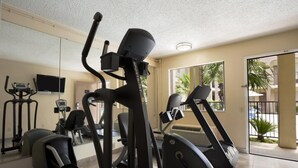 Een sportschool met diverse fitnessapparaten, een televisie en uitzicht op buiten door een glazen deur.