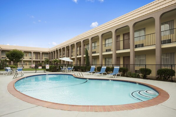 A hotel with a swimming pool, lounge chairs, and a covered patio area.