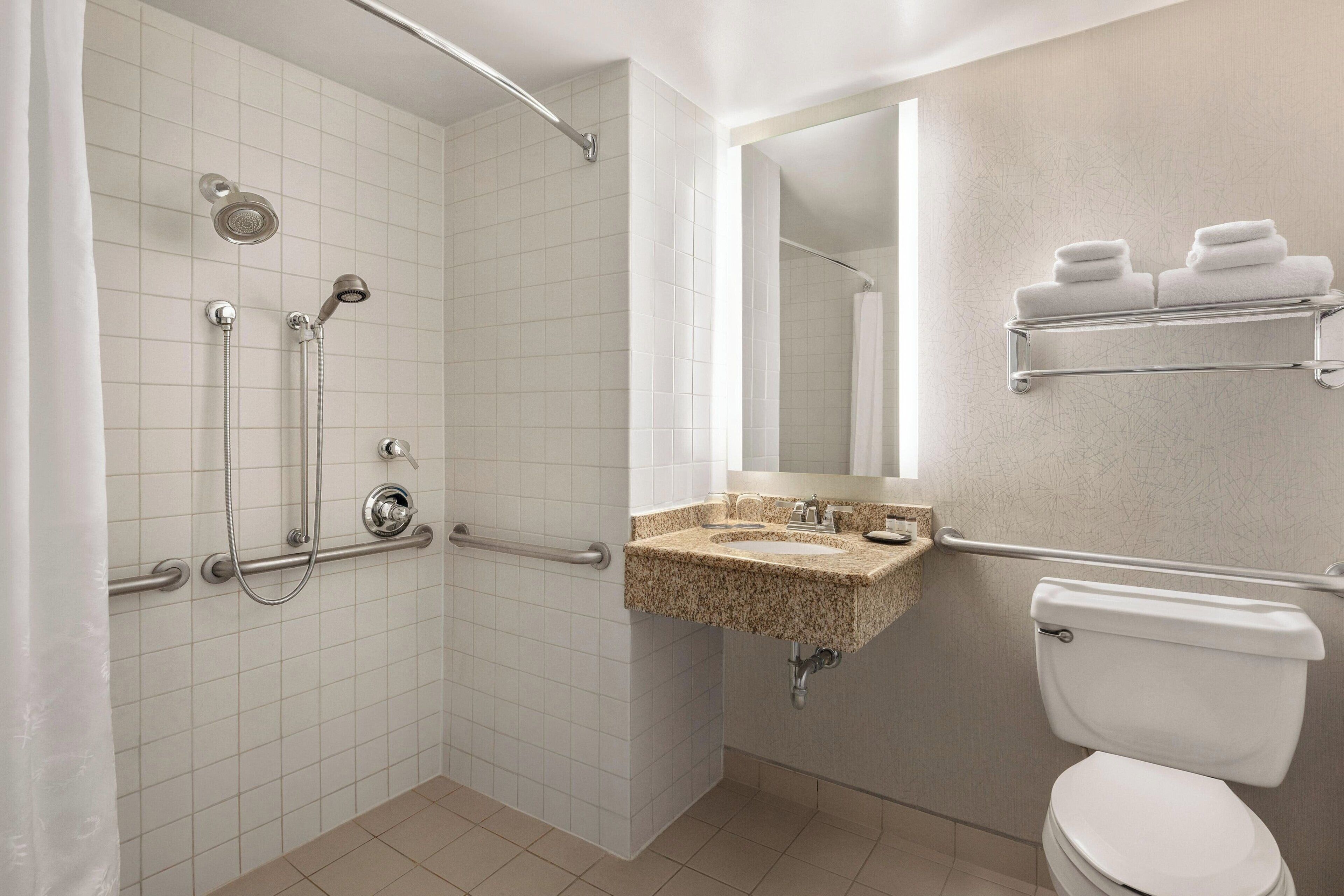 A bathroom with a walk-in shower, grab bars, a sink with a mirror, and a toilet.