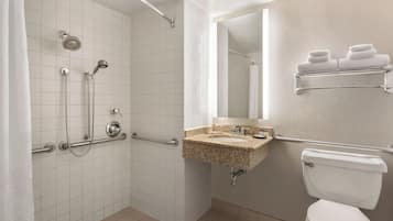 A bathroom with a walk-in shower, grab bars, a sink with a mirror, and a toilet.