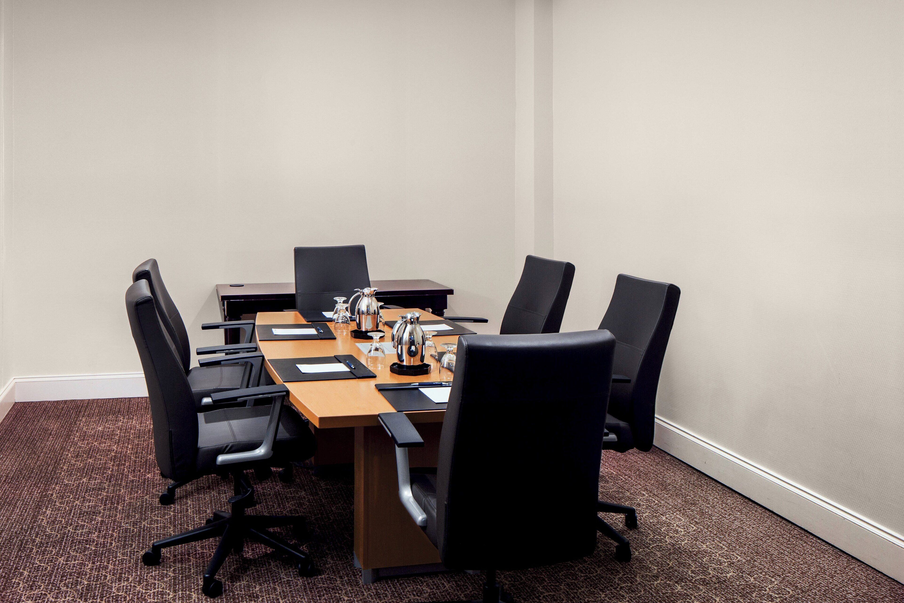 A conference room with a rectangular table, six black chairs, and a coffee pot.