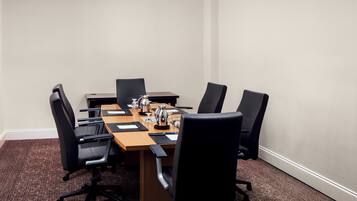 A conference room with a rectangular table, six black chairs, and a coffee pot.
