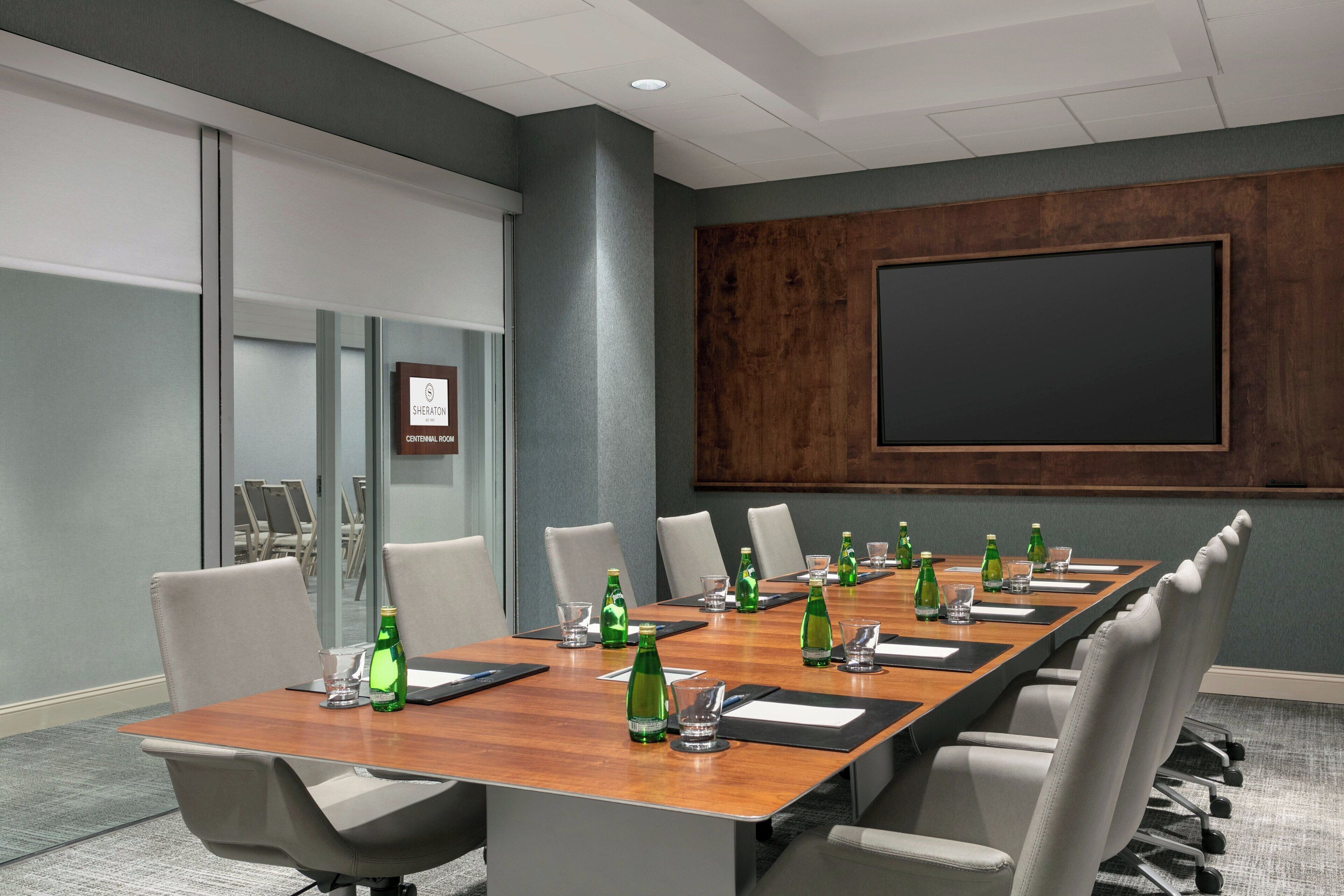 A conference room with a long table, chairs, a projector screen, and a Sheraton sign.