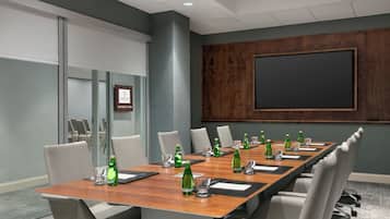 Un salón de conferencias con una larga mesa, sillas, una pantalla de proyector y un letrero de Sheraton.