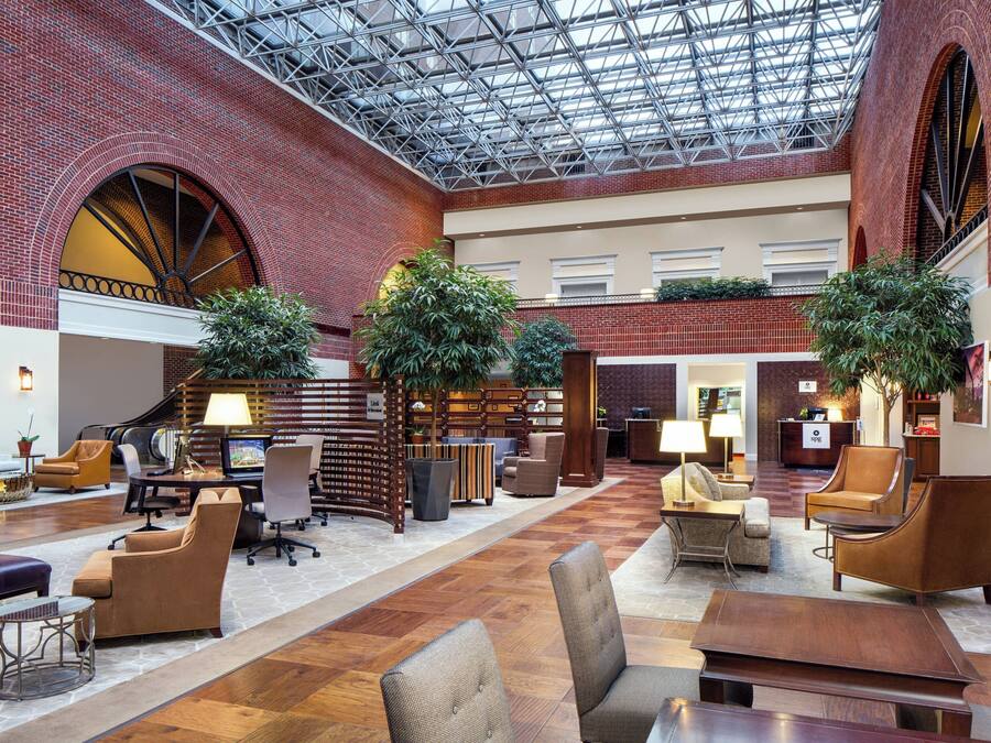 A spacious lobby with a high ceiling, brick walls, and multiple seating areas.