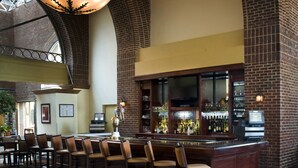 A bar area with a brick wall, bar stools, a counter with a cash register, and a large chandelier.