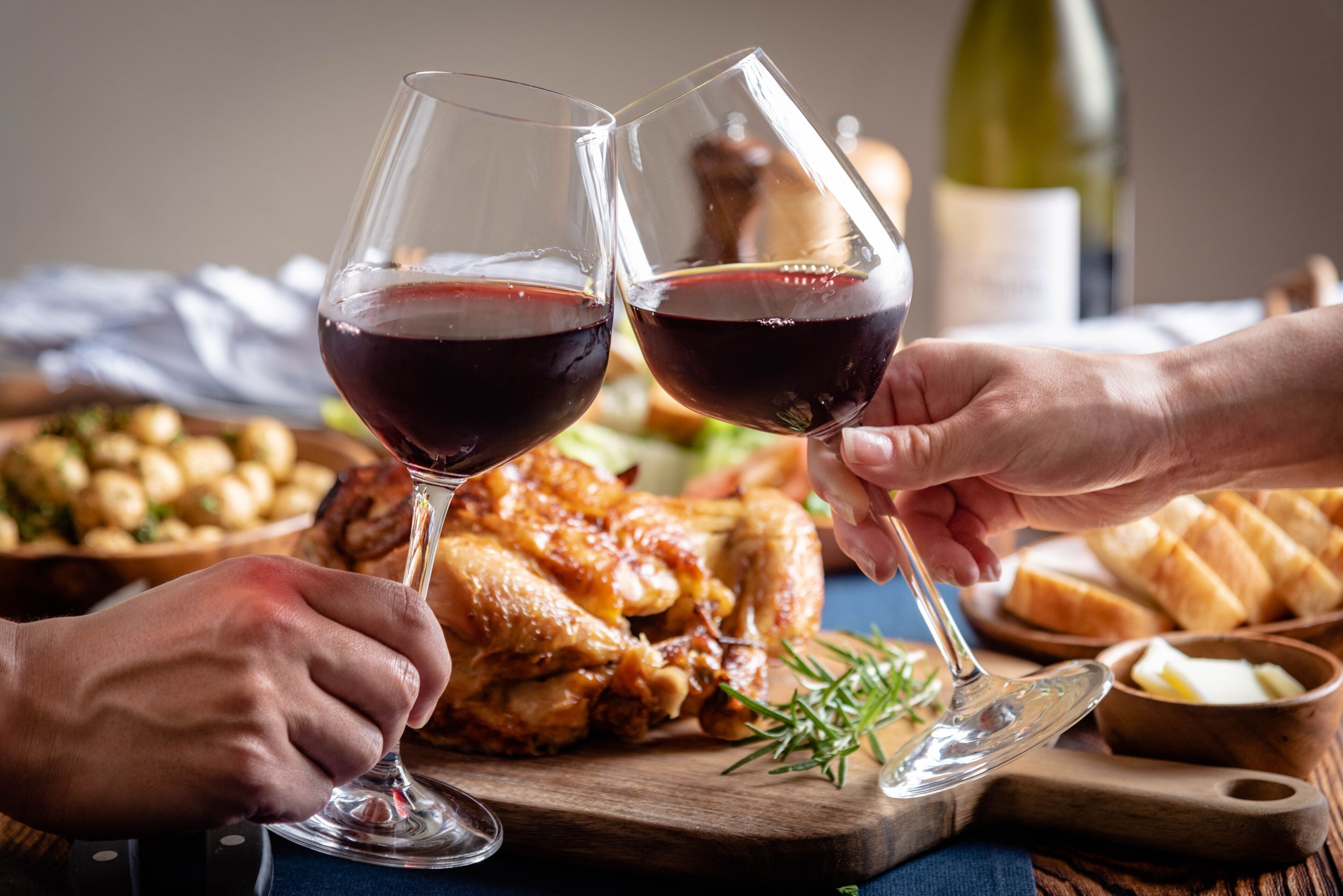 A dining table with a roasted chicken, bread, and a bottle of wine.