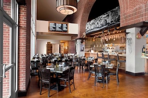 A restaurant with brick walls, wooden tables, and hanging lights. - Sheraton Raleigh Hotel (Raleigh)