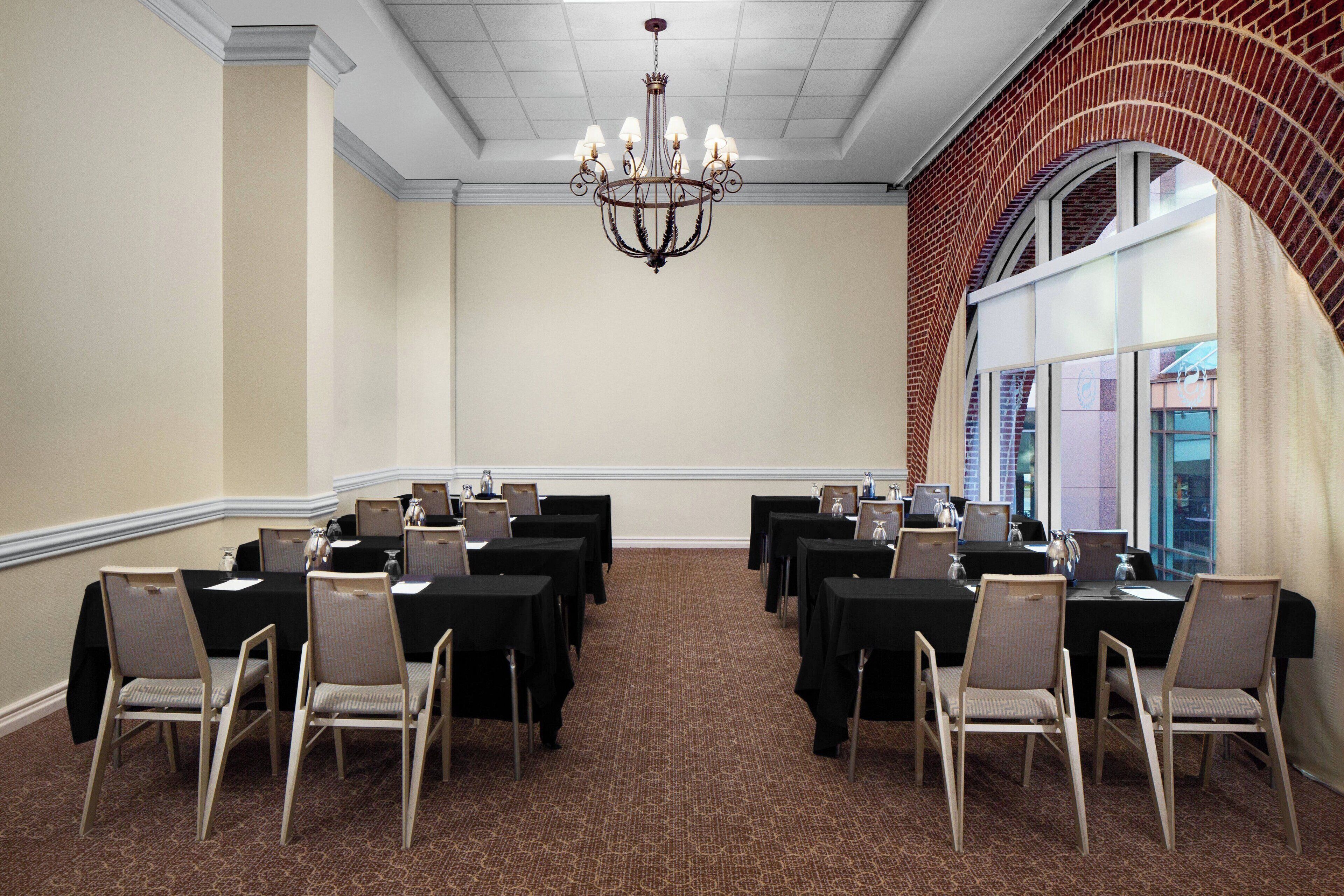 A conference room with tables and chairs, a chandelier, and a brick wall.